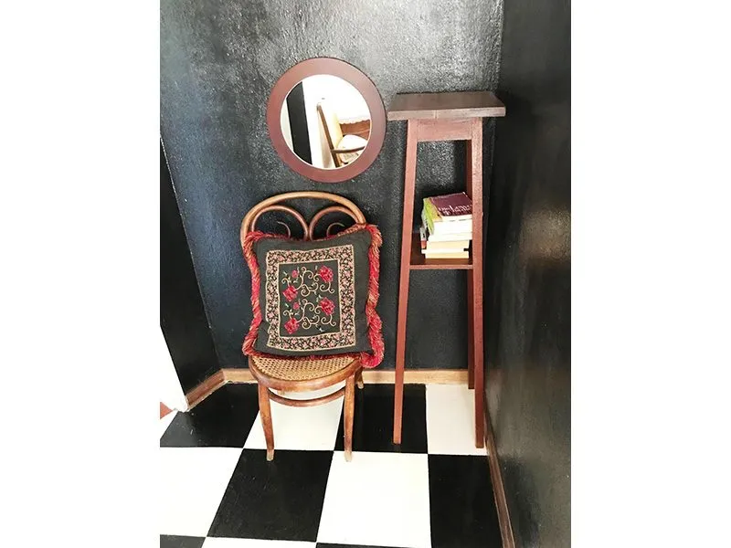 Chair with embroidered cushion round mirror and wooden shelf in a dark room