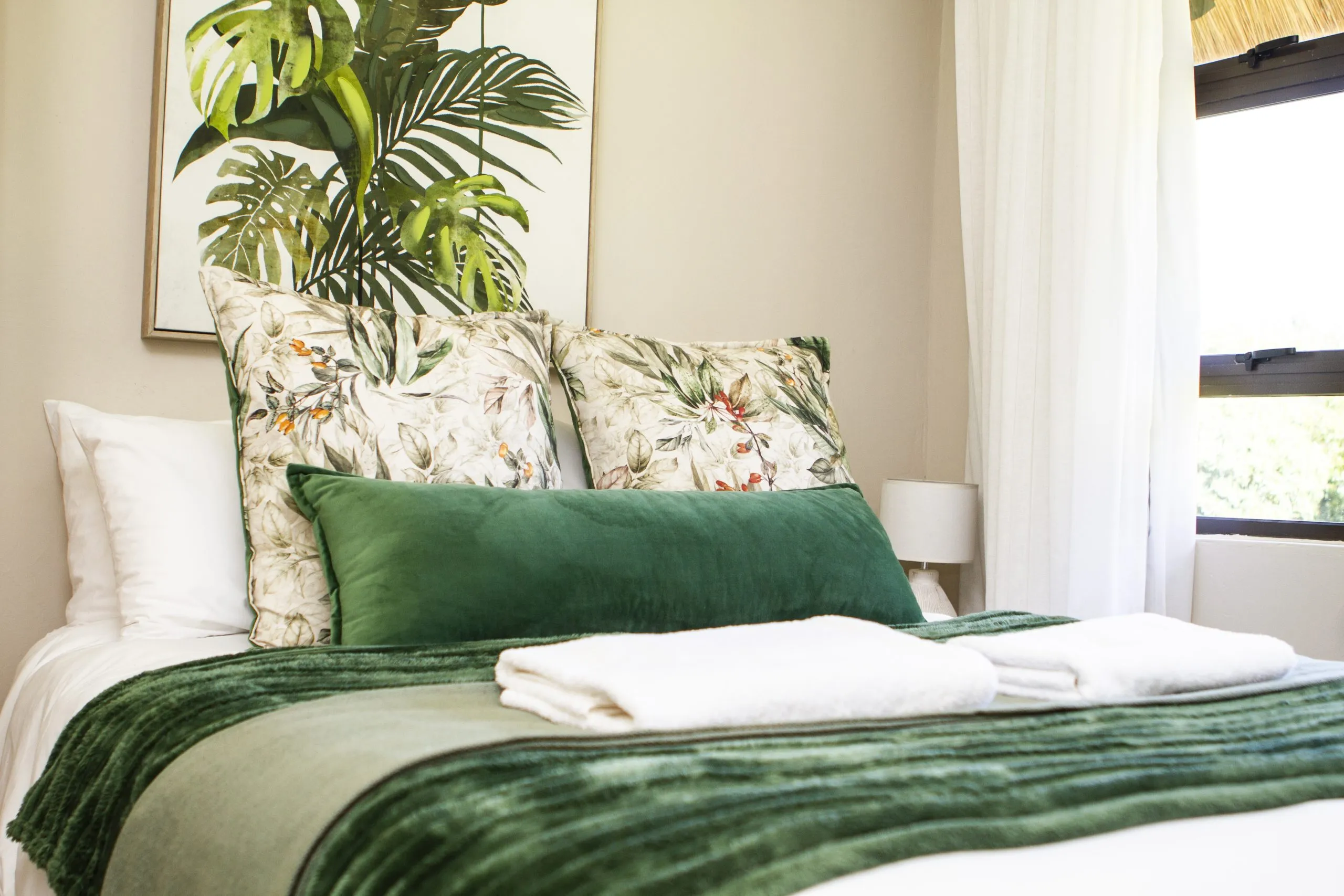 Cozy bed with green and white pillows and blankets in a bright room