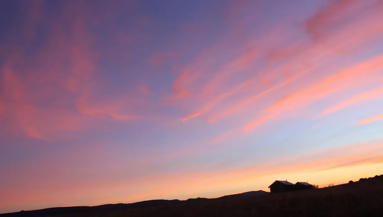 Sunset with pink and purple sky over a silhouette of a house and fields