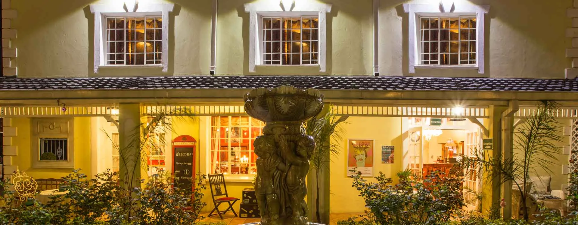 Colonialstyle building with illuminated windows a fountain and lush greenery at night