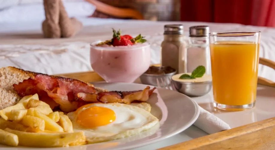 Breakfast tray with eggs bacon fruit juice and condiments on a bed