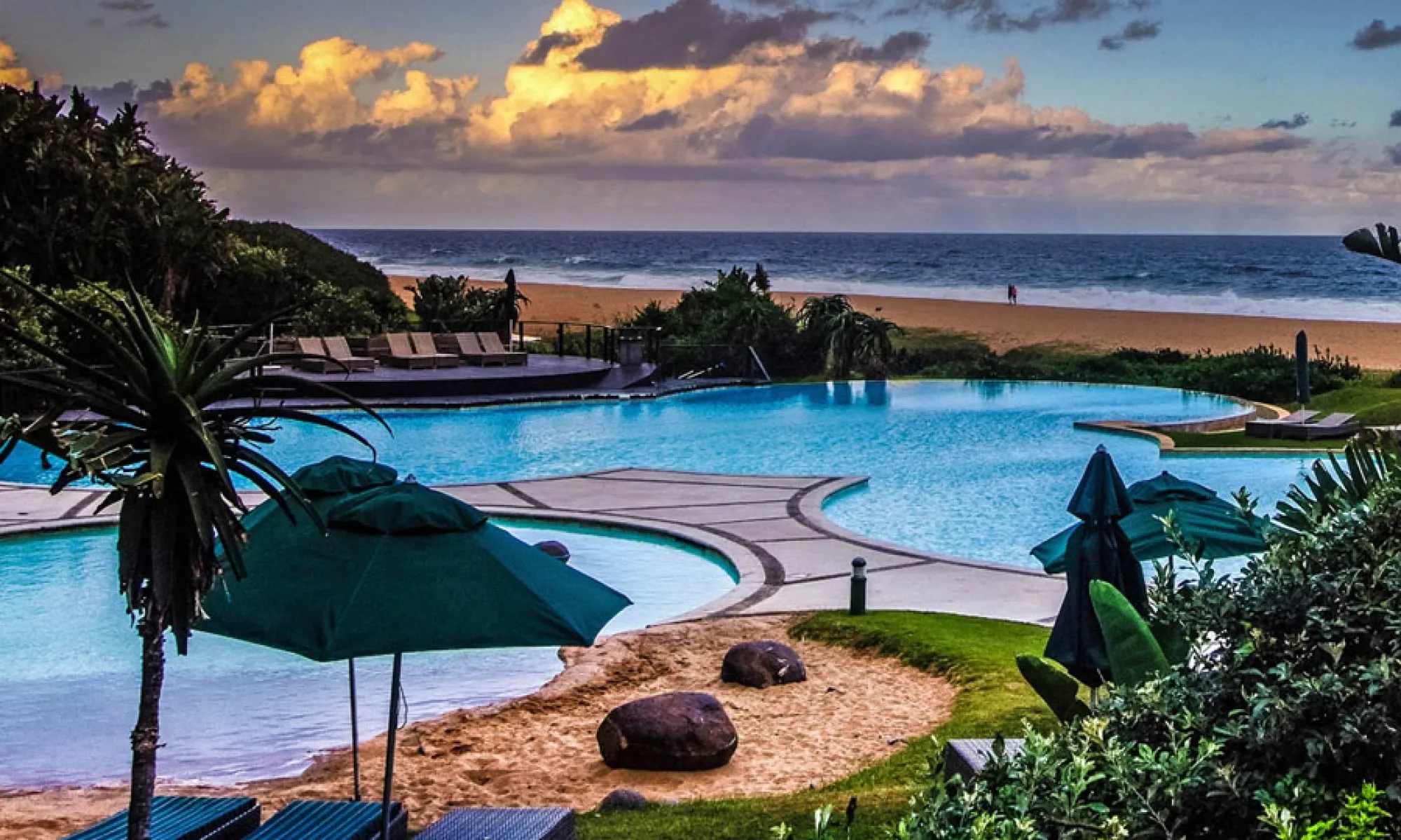 Resort with pools lounge chairs umbrellas and ocean view under a cloudy sky