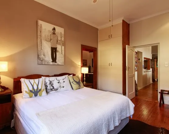 Bedroom with large bed pillows wardrobe and wooden floor leading to a hallway