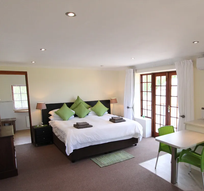 Bedroom with large bed green pillows and dining table with green chairs