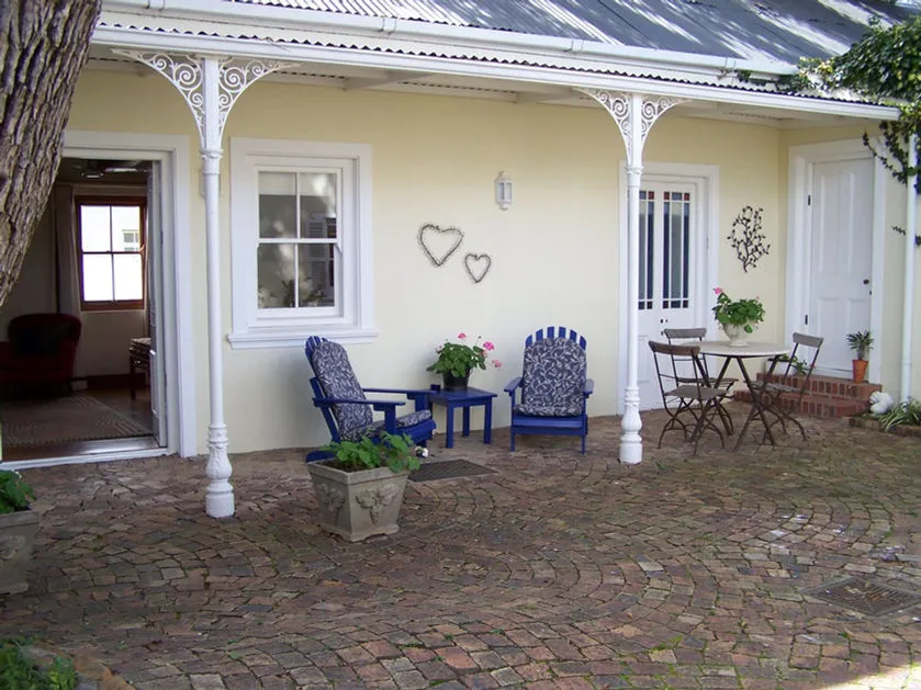 Two blue chairs on a brick patio under a covered porch with potted plants