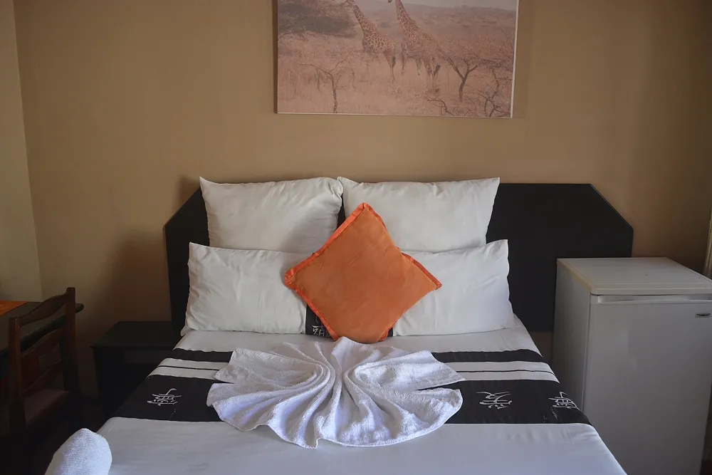 Neatly made bed with orange pillow and folded towel in a bedroom