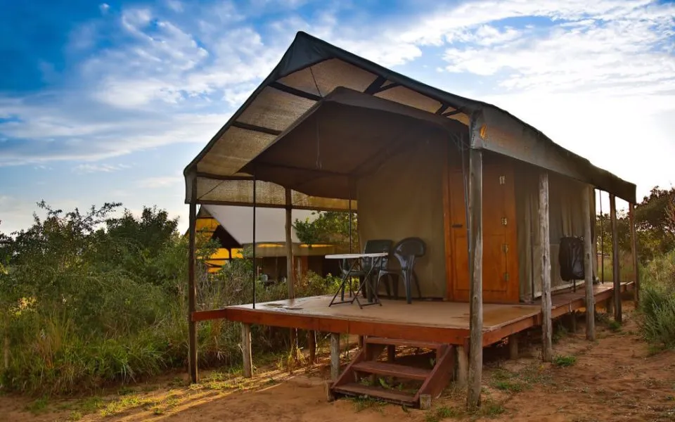 Wooden cabin with a porch and chairs in a natural setting under a blue sky
