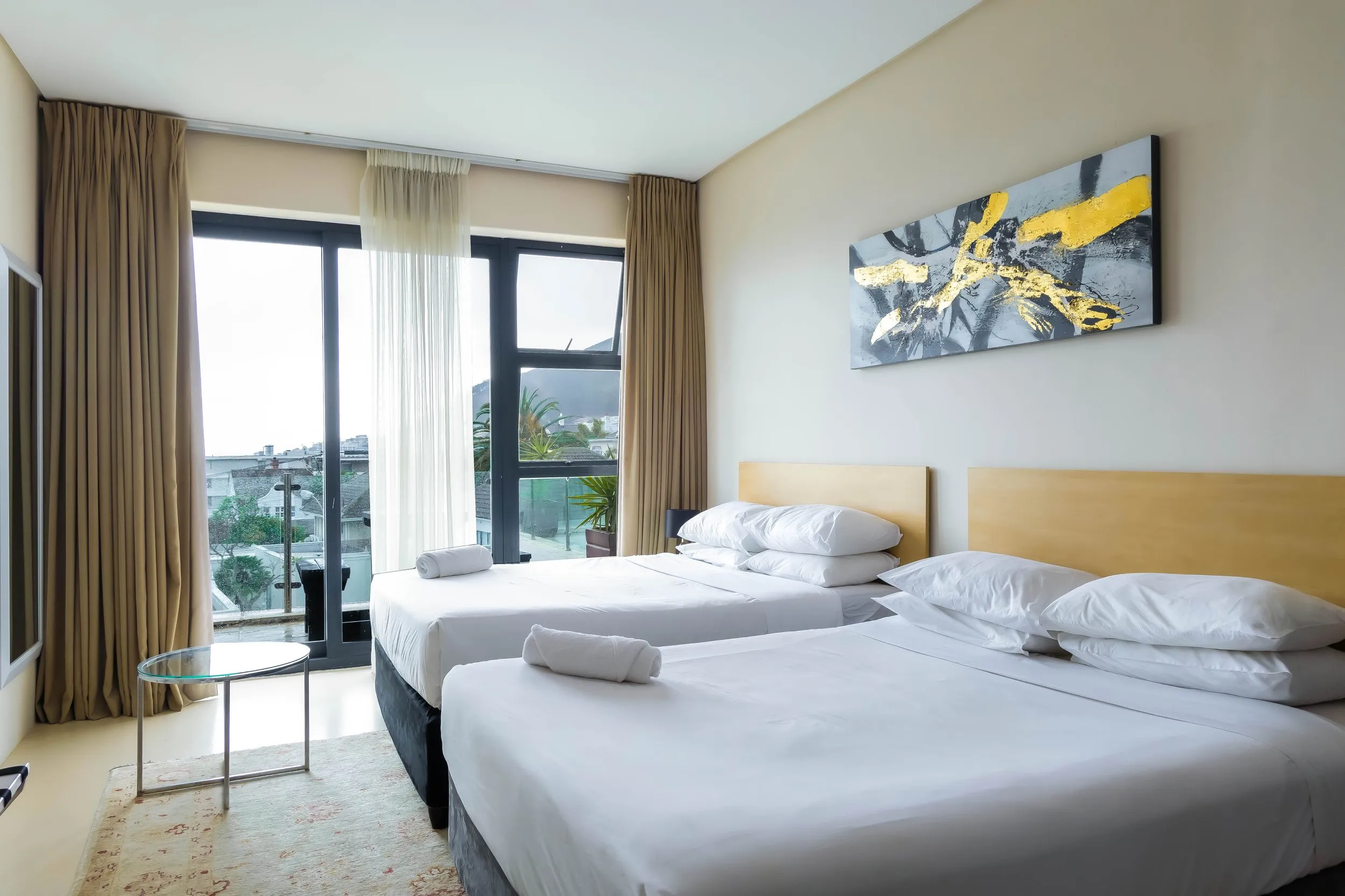 Two beds in a modern hotel room with large windows and abstract wall art