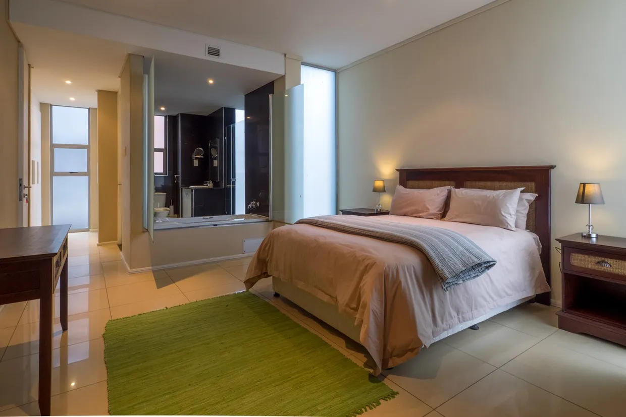 Bedroom with a large bed green rug and an attached bathroom visible through a mirror