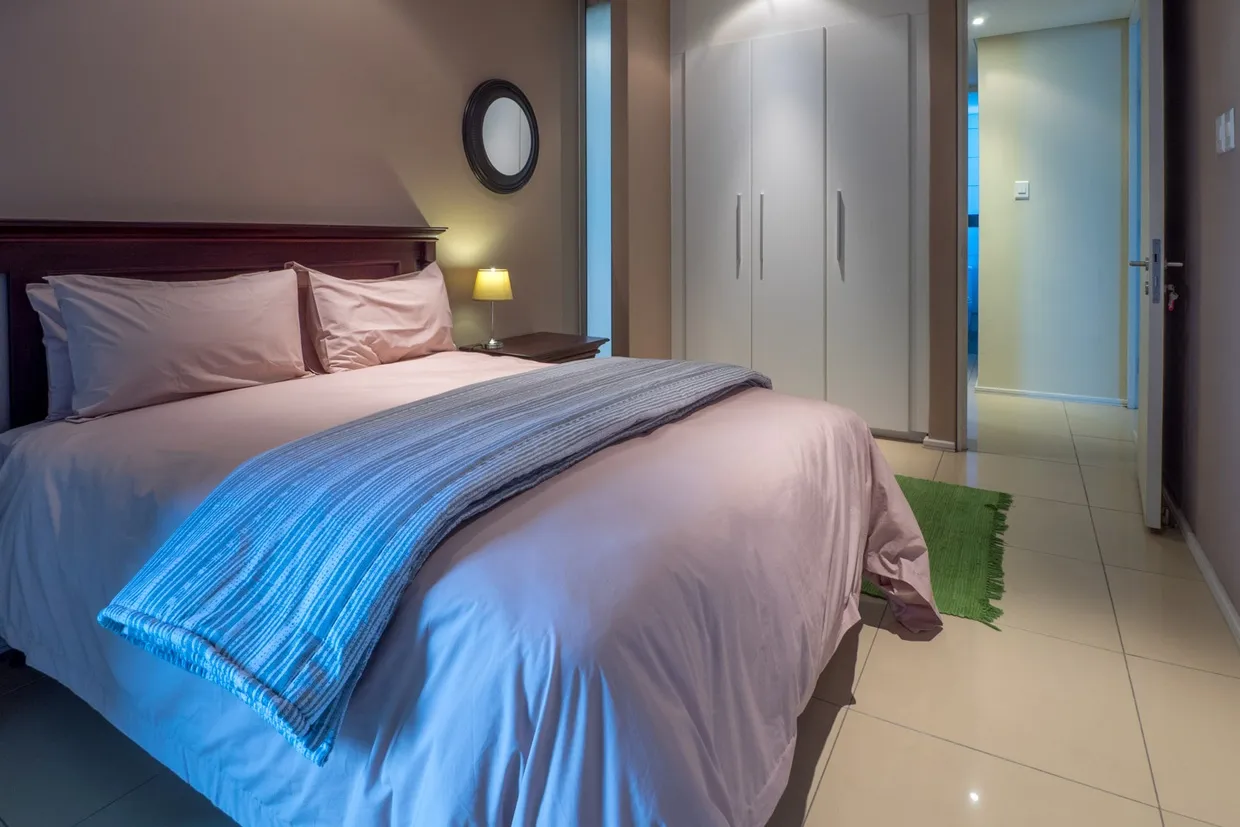 Bedroom with a neatly made bed bedside lamp and open door to hallway