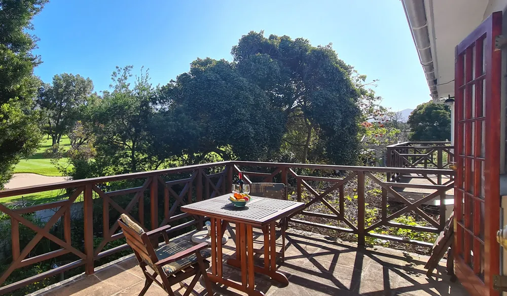 Wooden balcony with table and chairs overlooking a lush garden and golf course