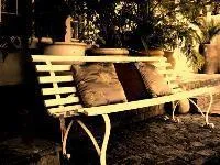 White bench with cushions in a garden setting with potted plants