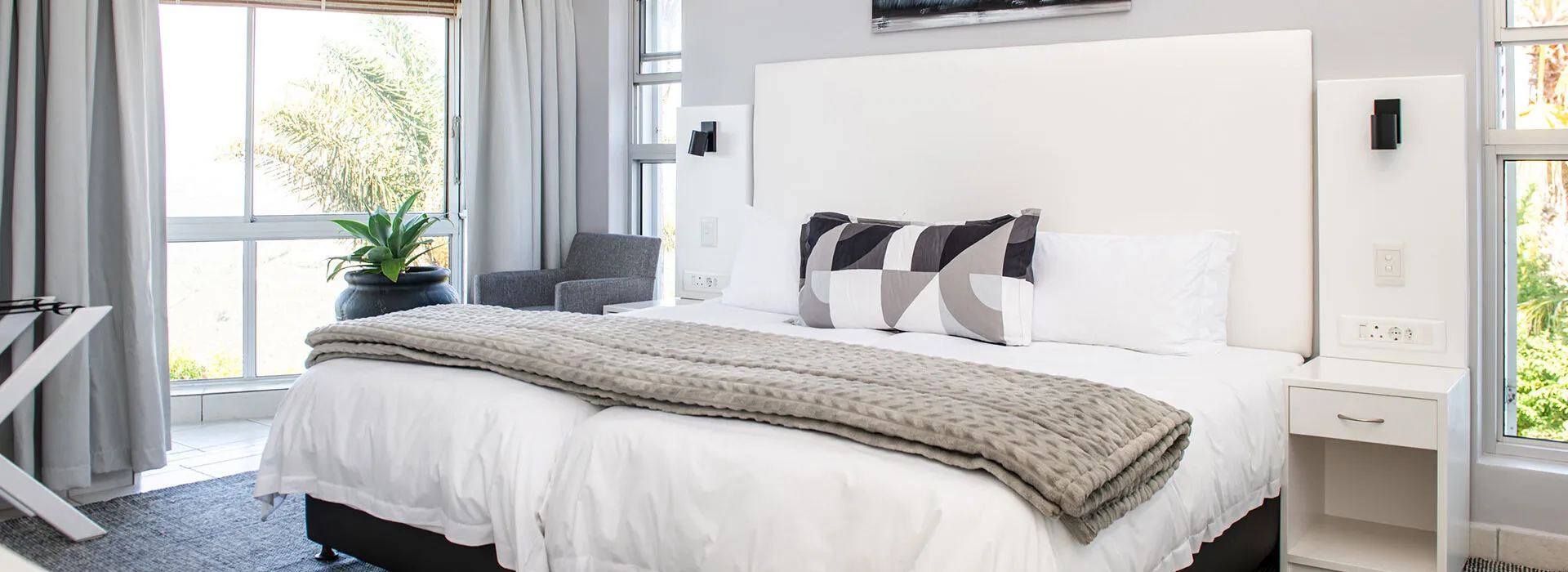 Bright bedroom with large bed white headboard and large windows with curtains