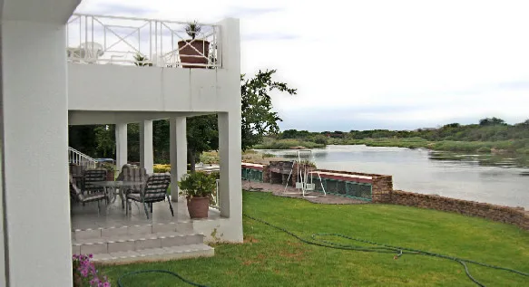 Modern house with patio overlooking a river surrounded by green lawn