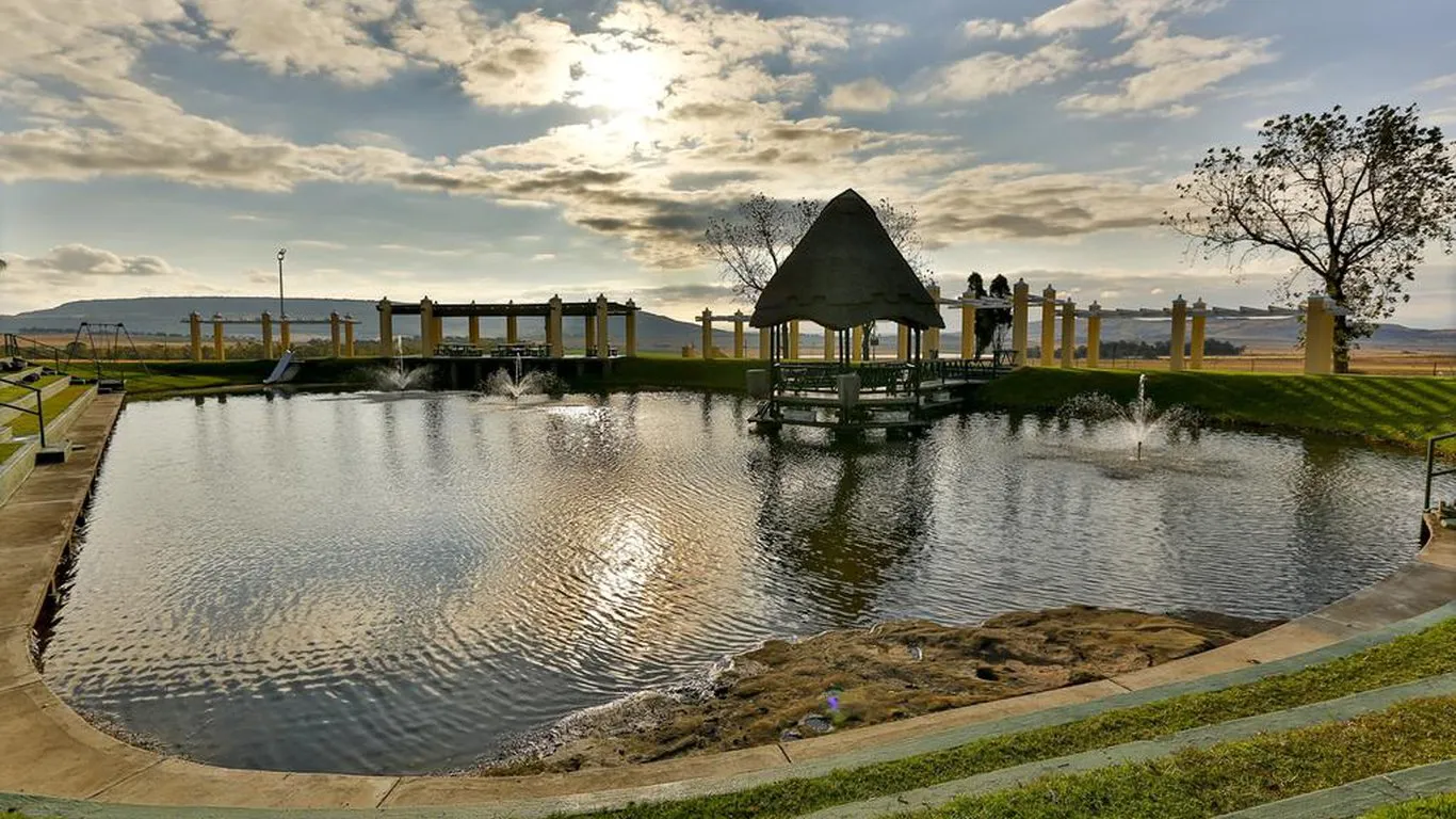 Pond with gazebo bridge and fountains in a park setting under a cloudy sky