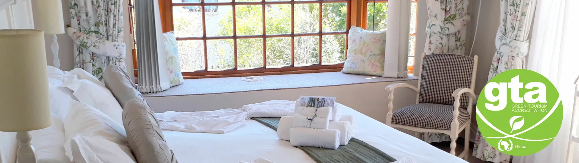 Bedroom with large window white bed and armchair featuring a green ecofriendly logo