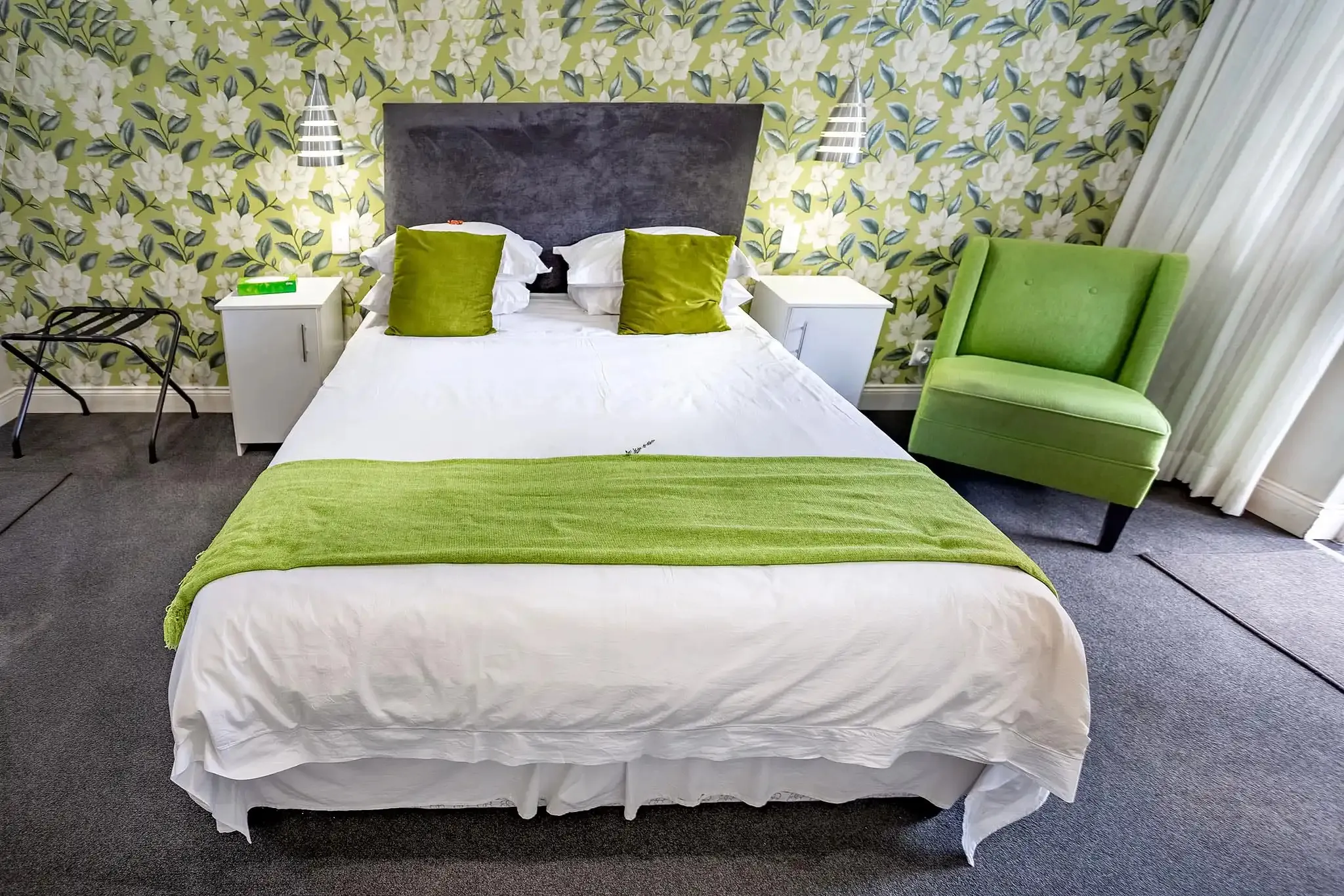 Bedroom with a bed green pillows green throw and green armchair on floral wallpaper