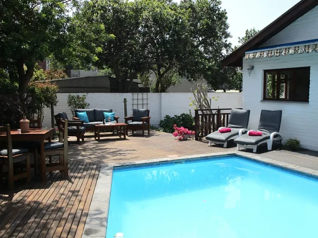 Wooden deck with pool lounge chairs and outdoor seating area surrounded by greenery