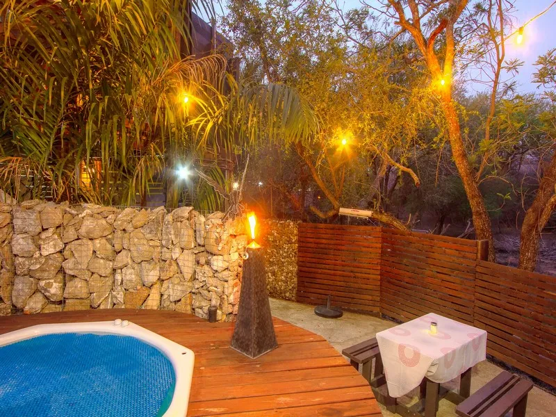 Outdoor patio with pool wooden deck lit torch and string lights at night