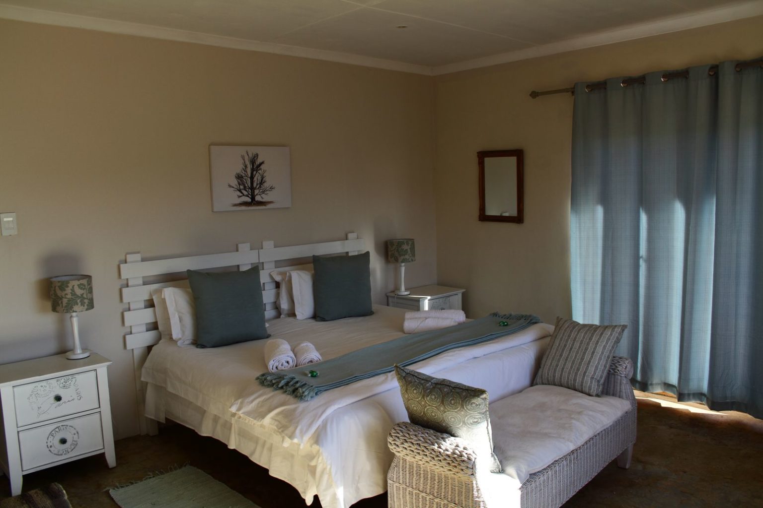 Bedroom with a large bed, side tables, and a chaise lounge by a window.