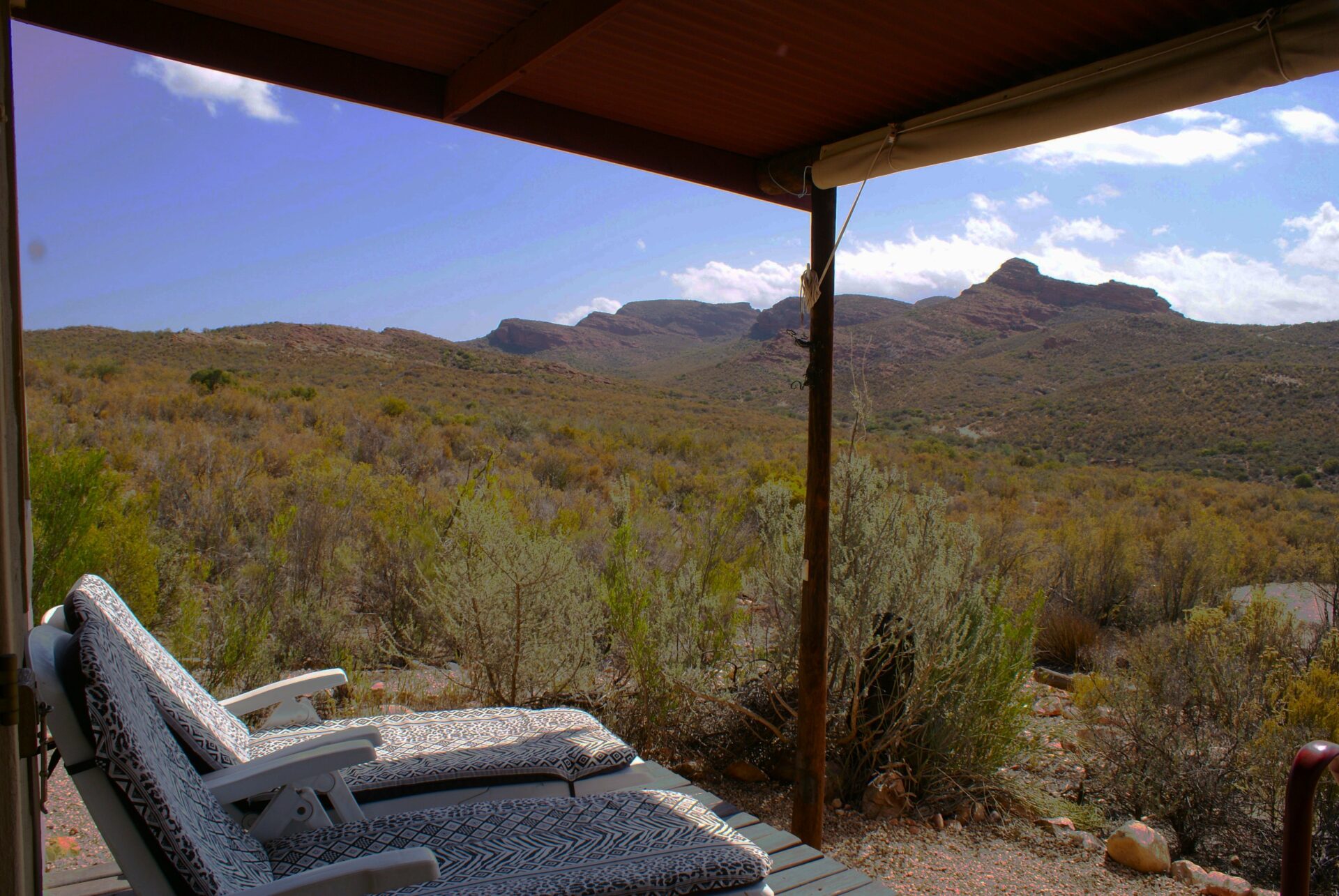 Two lounge chairs on a deck overlooking a mountainous desert landscape.