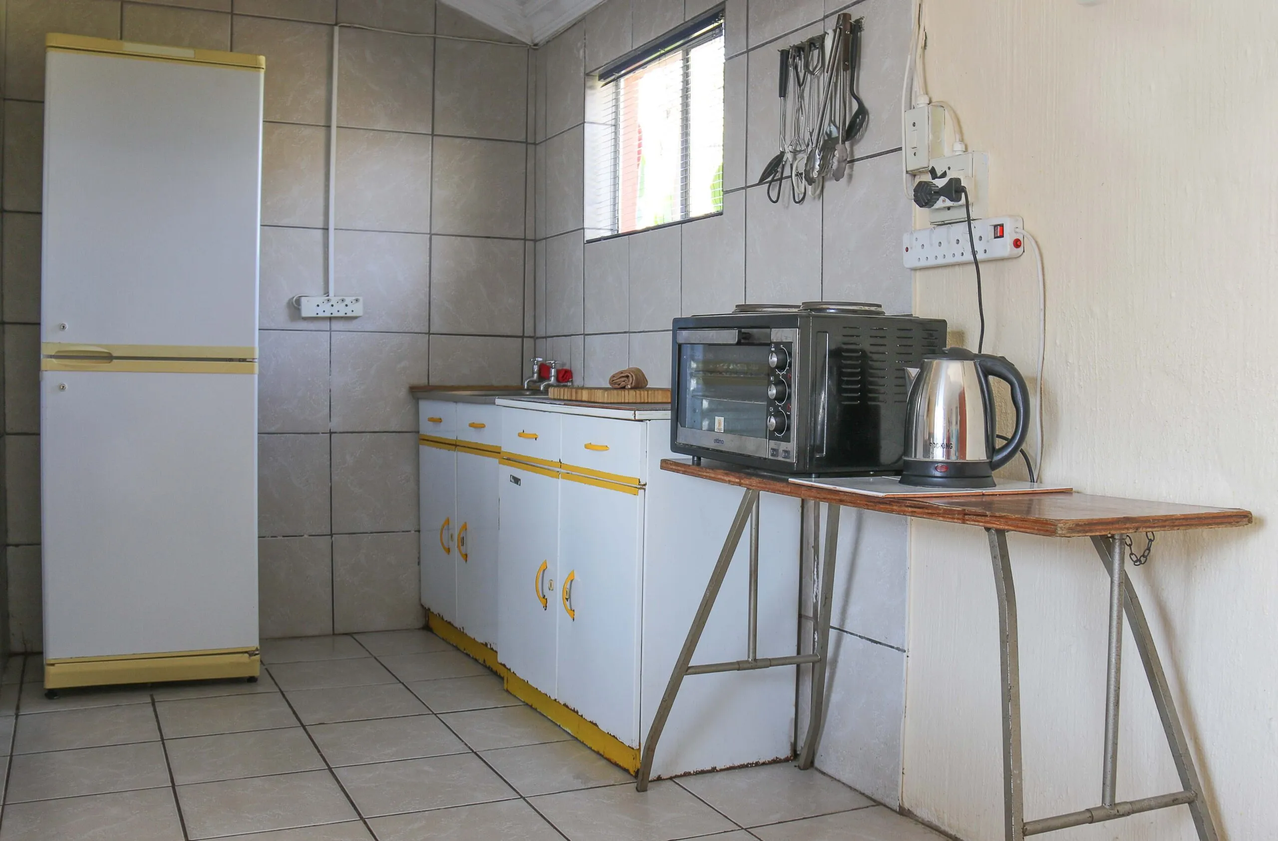 Small kitchen with white fridge microwave kettle and tiled walls