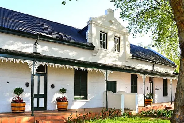 White house with blue roof green shutters and potted plants on the porch