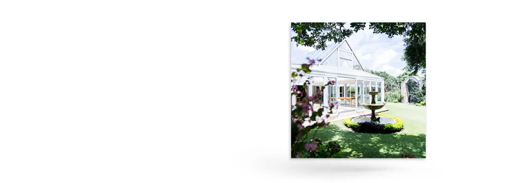 White greenhouse with a fountain in a lush garden on a sunny day