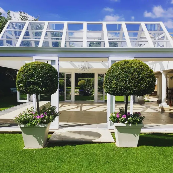 White conservatory with potted plants and topiary trees on a green lawn
