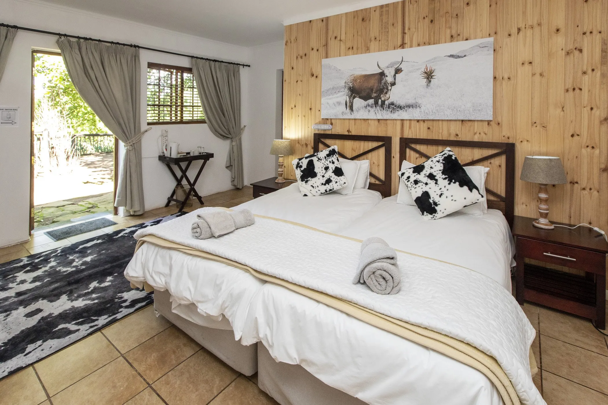 Bedroom with two beds wooden walls cow print pillows and a large window