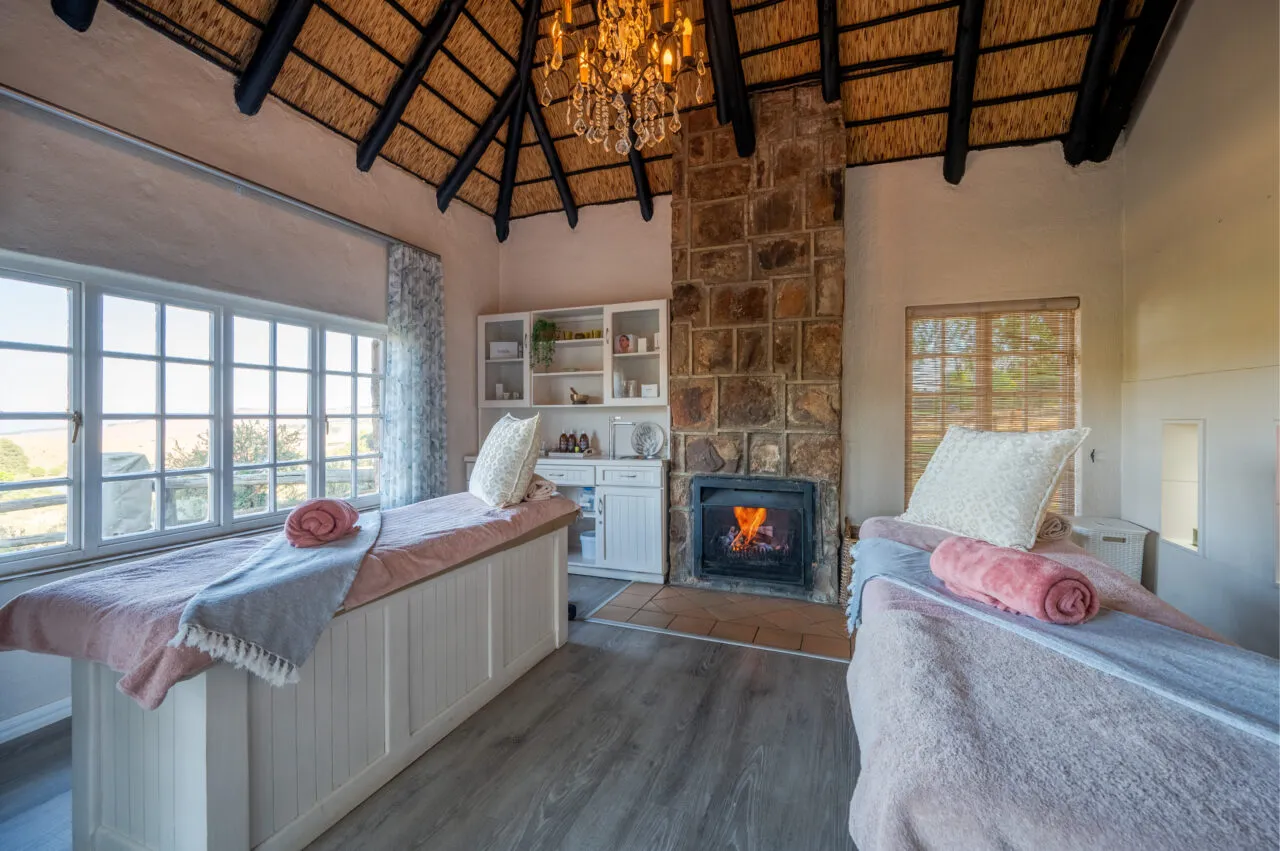 Two massage tables in a cozy room with a fireplace and large windows