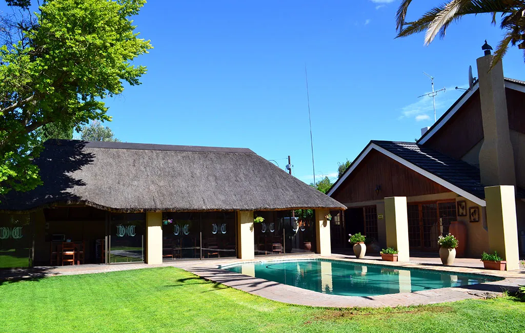 House with a thatched roof and swimming pool in a sunny garden