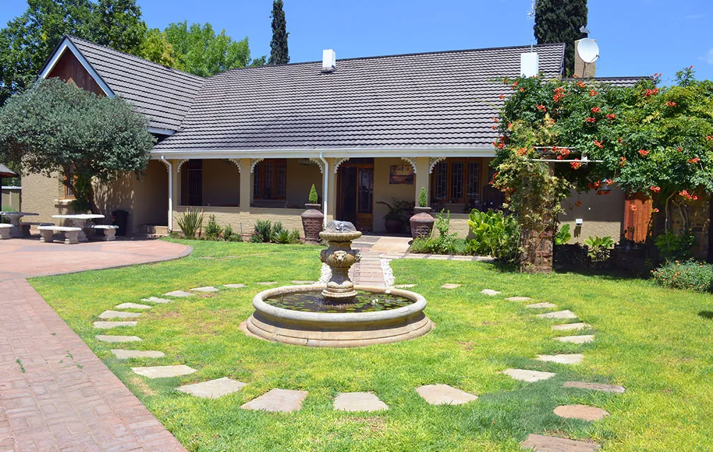 Singlestory house with tiled roof circular fountain and garden with stone path