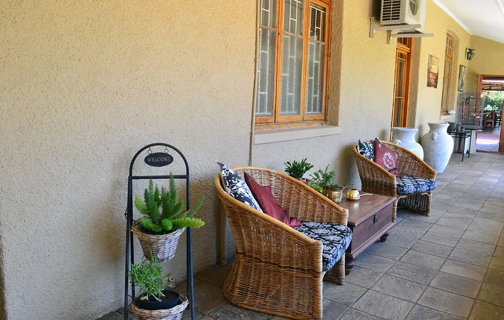 Wicker chairs with cushions on a tiled patio next to a house wall