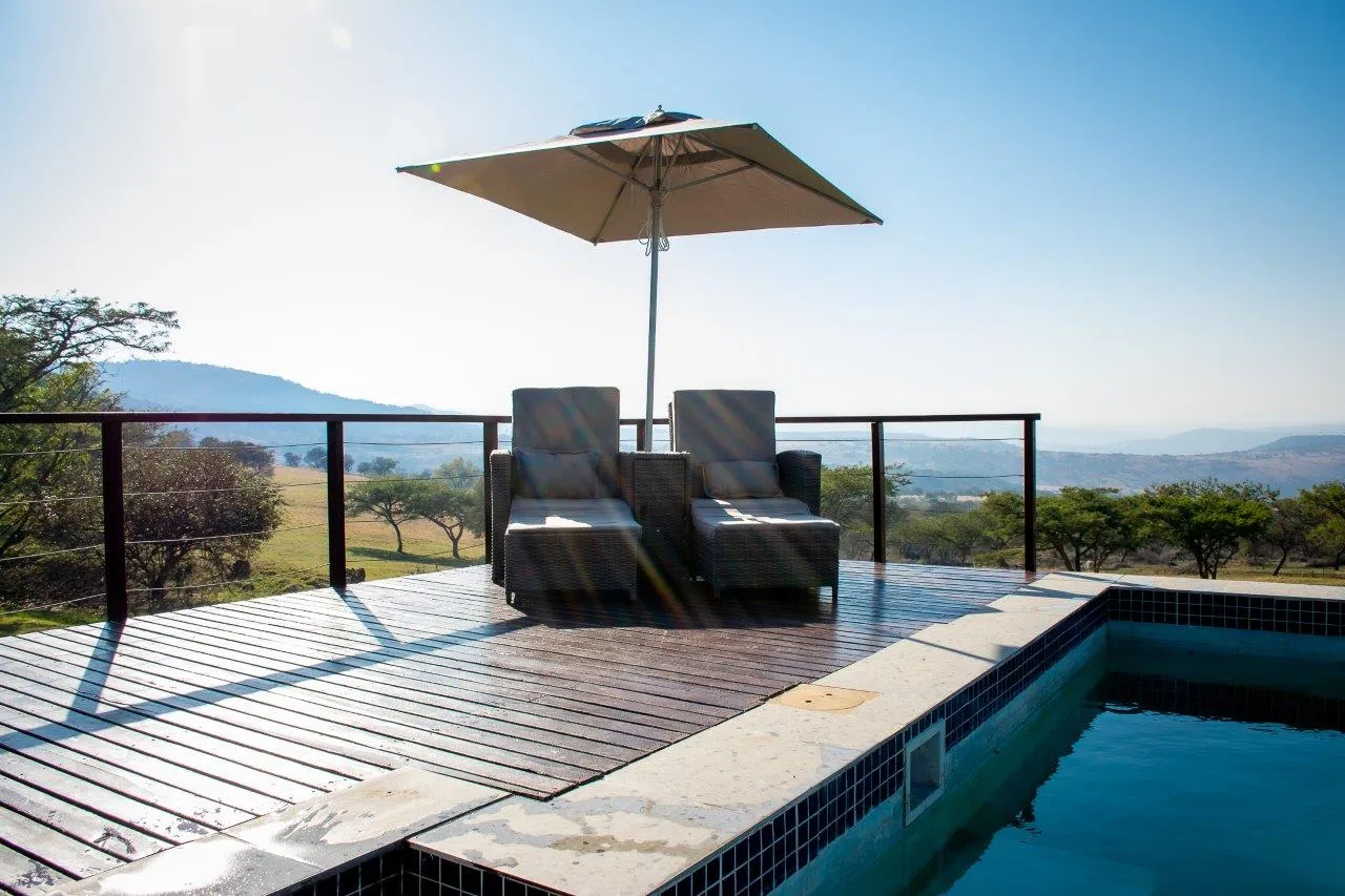Two lounge chairs under an umbrella by a pool with a scenic view