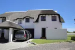 White house with a thatched roof and a car parked in front