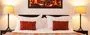 A bed with red pillows two lamps and a painting above it