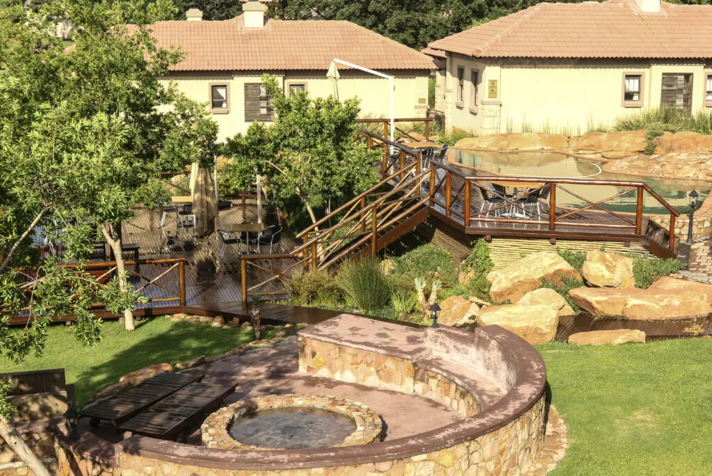 Garden with stone fire pit wooden bridge and surrounding buildings with trees