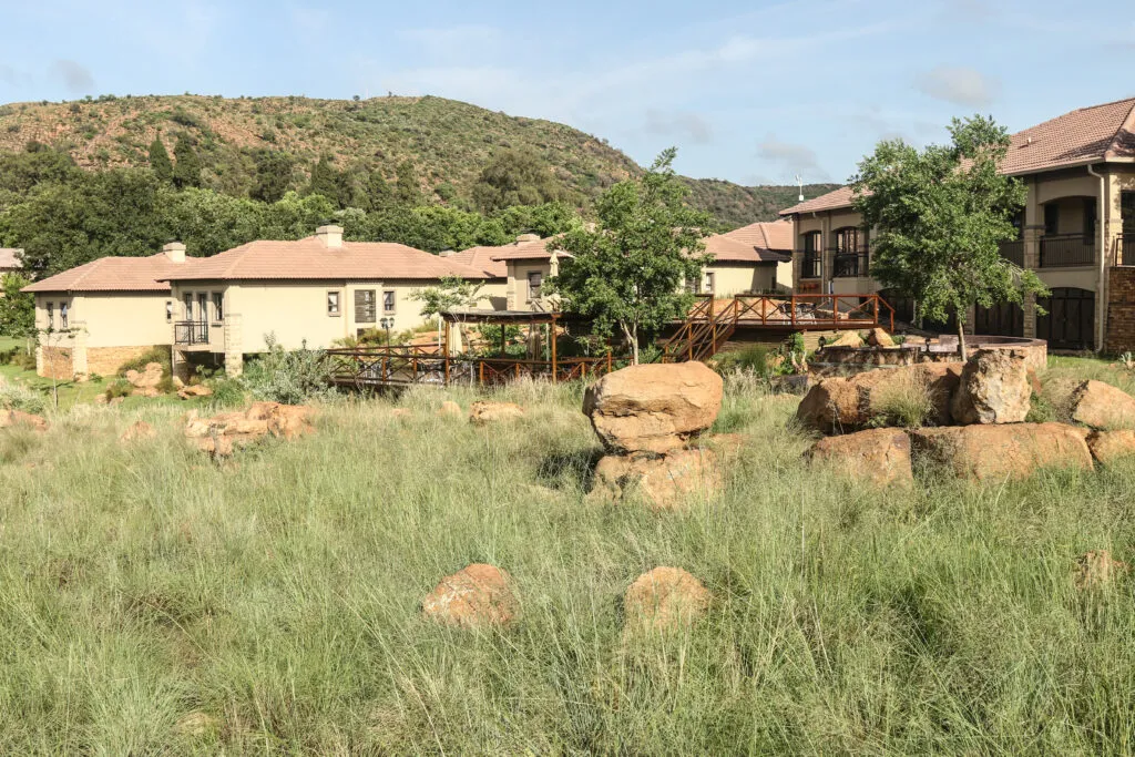 Houses with red roofs surrounded by grassy area and large rocks with hills in background