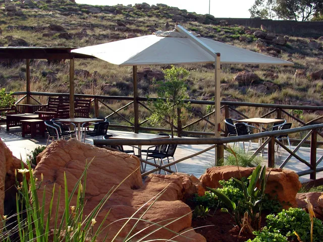 Outdoor seating area with tables chairs and a large umbrella on a rocky terrace