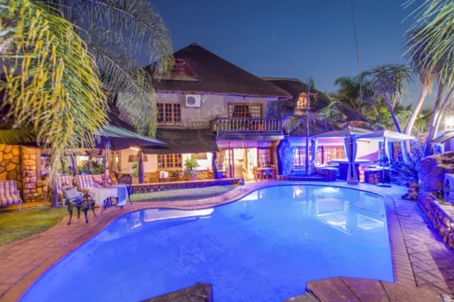 Night view of a house with an illuminated swimming pool and palm trees
