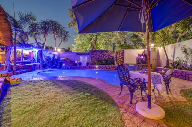 Evening backyard scene with pool umbrella table and chairs illuminated by lights