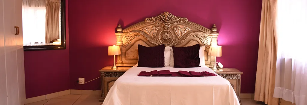 Ornate bed with red pillows in a room with purple walls and white bedding