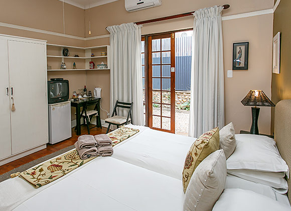 Cozy bedroom with two single beds, white curtains, and a small desk.