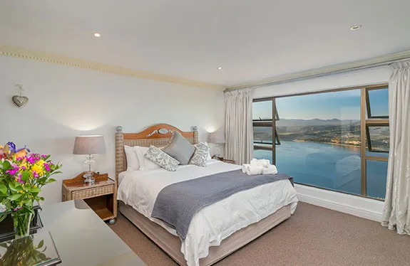 Bedroom with large window view of lake mountains and cloudy sky