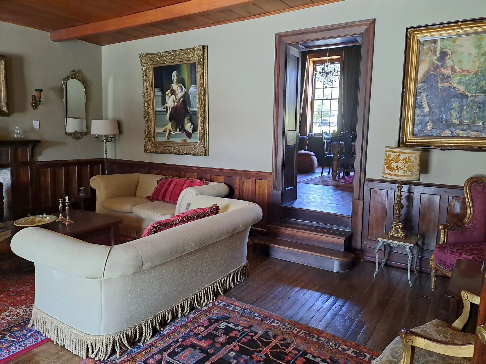 Cozy living room with ornate paintings wooden paneling and a doorway to another room
