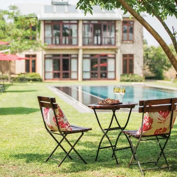 Two chairs and a table by a pool with a house in the background