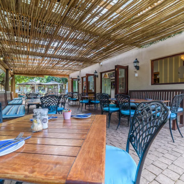 Outdoor seating area with wooden tables and chairs under a thatched roof