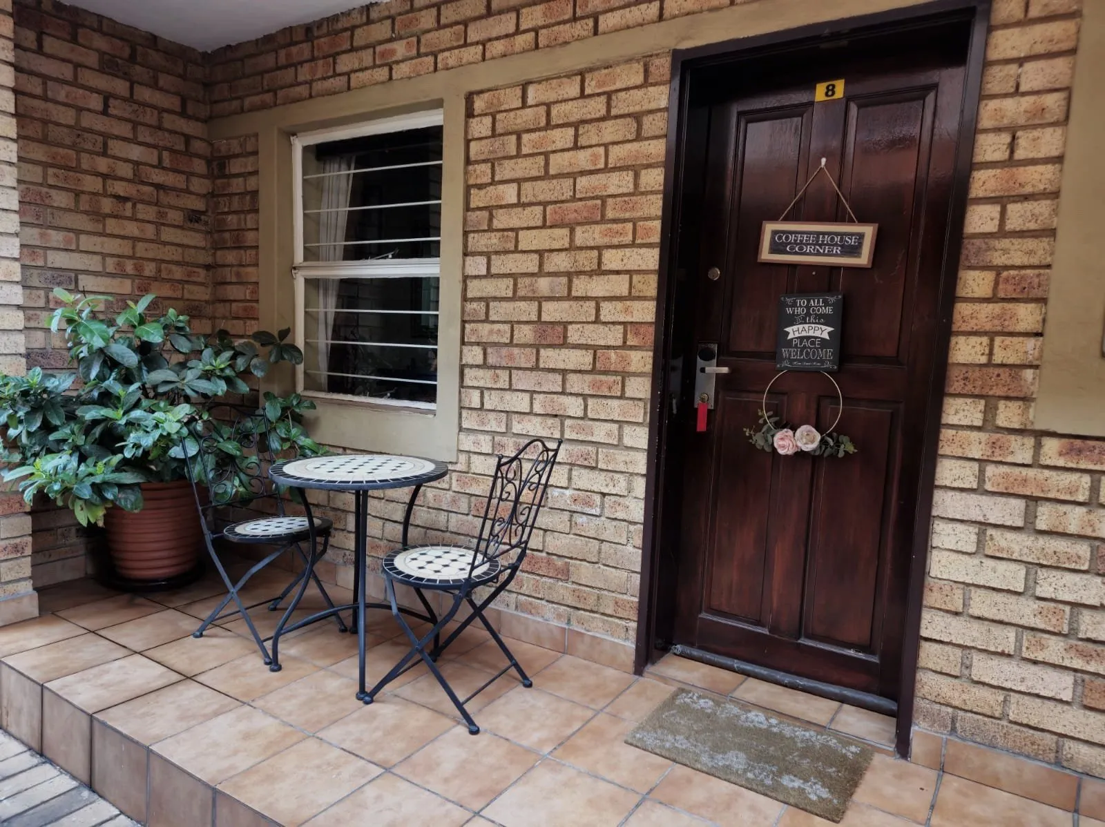 Brick wall with door potted plant and metal table and chairs on tiled porch