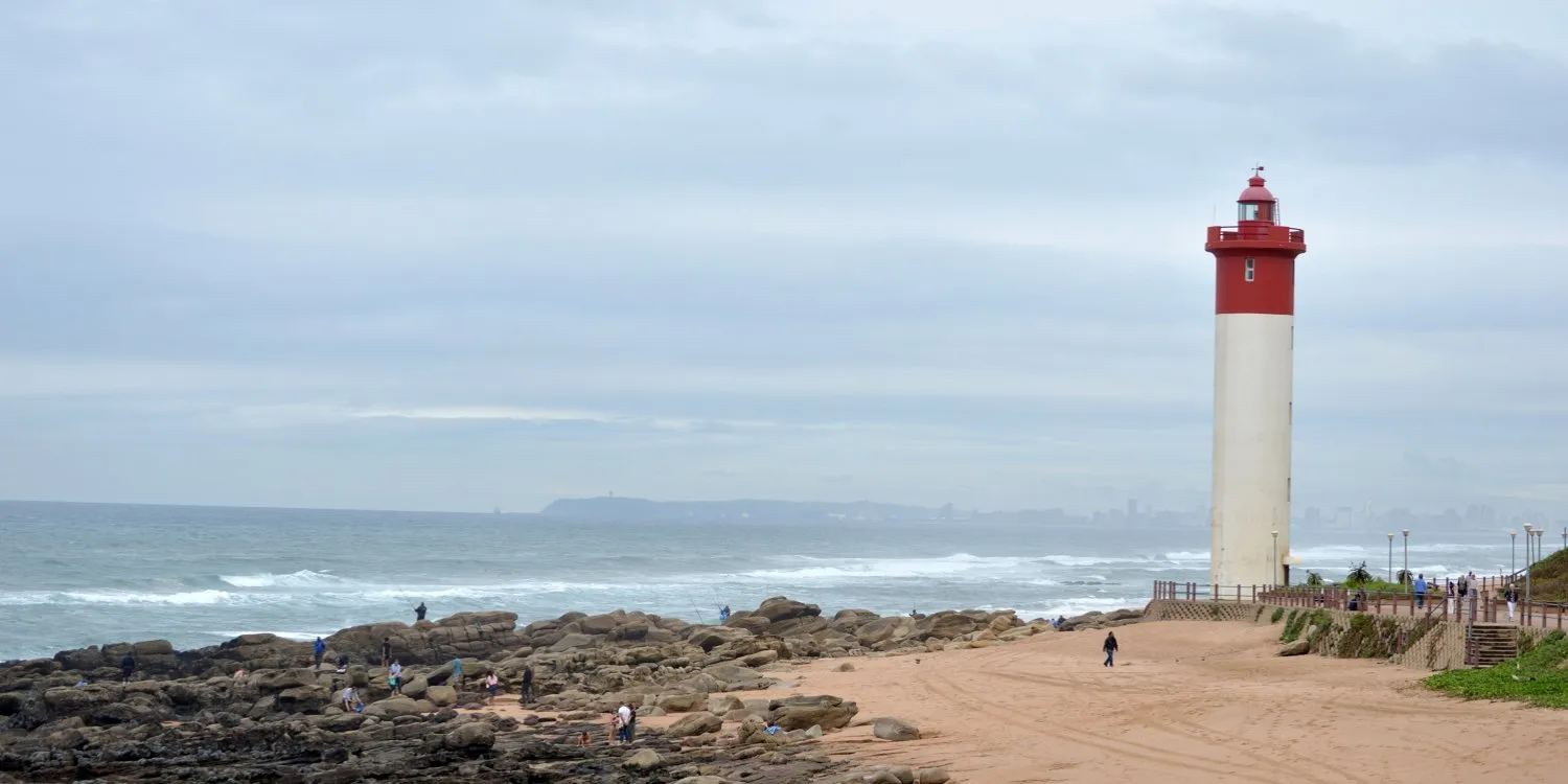 Lighthouse on a sandy beach with rocky shore and people walking
